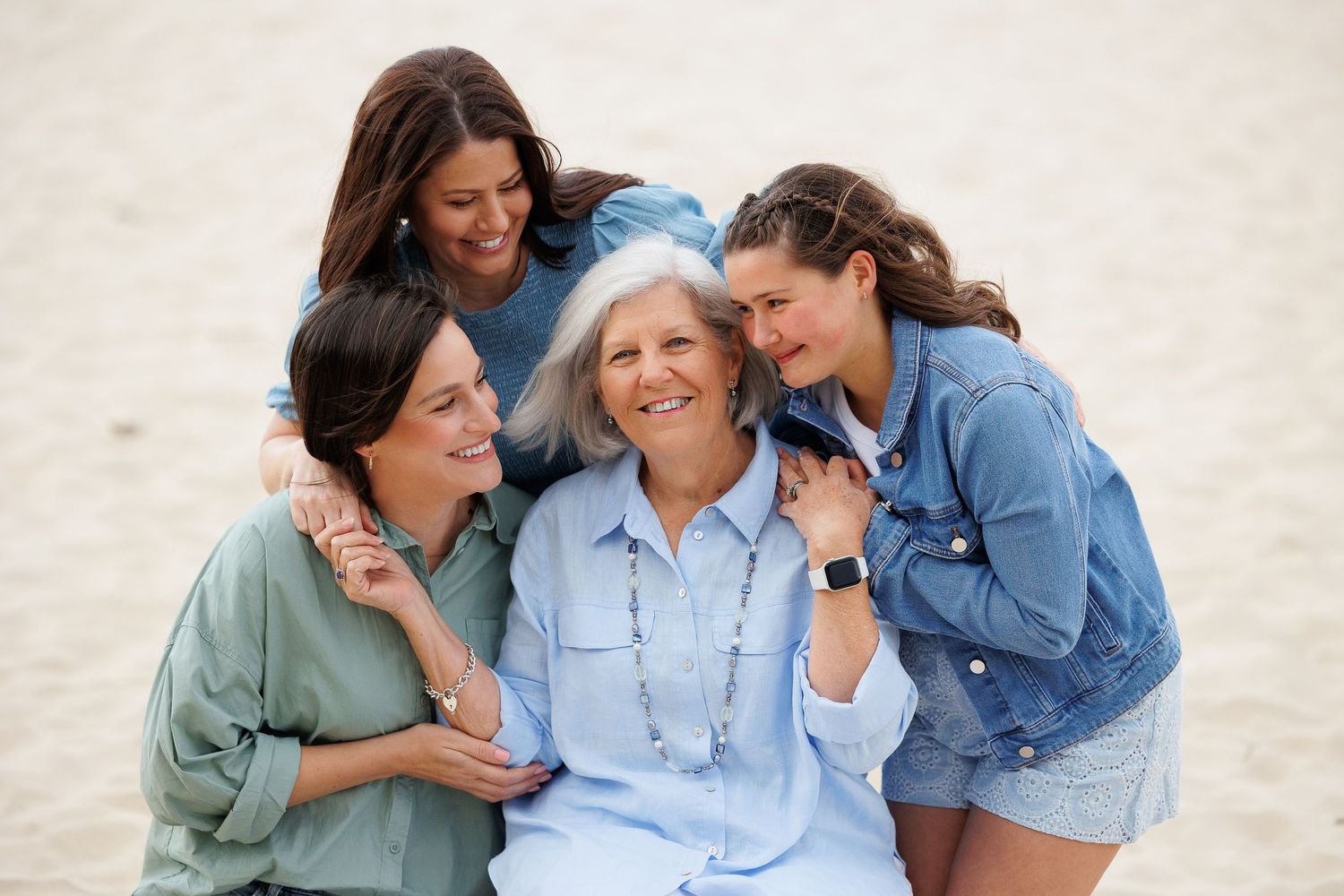 Four people sitting close together on sandy beach sharing joyful moment in casual attire.