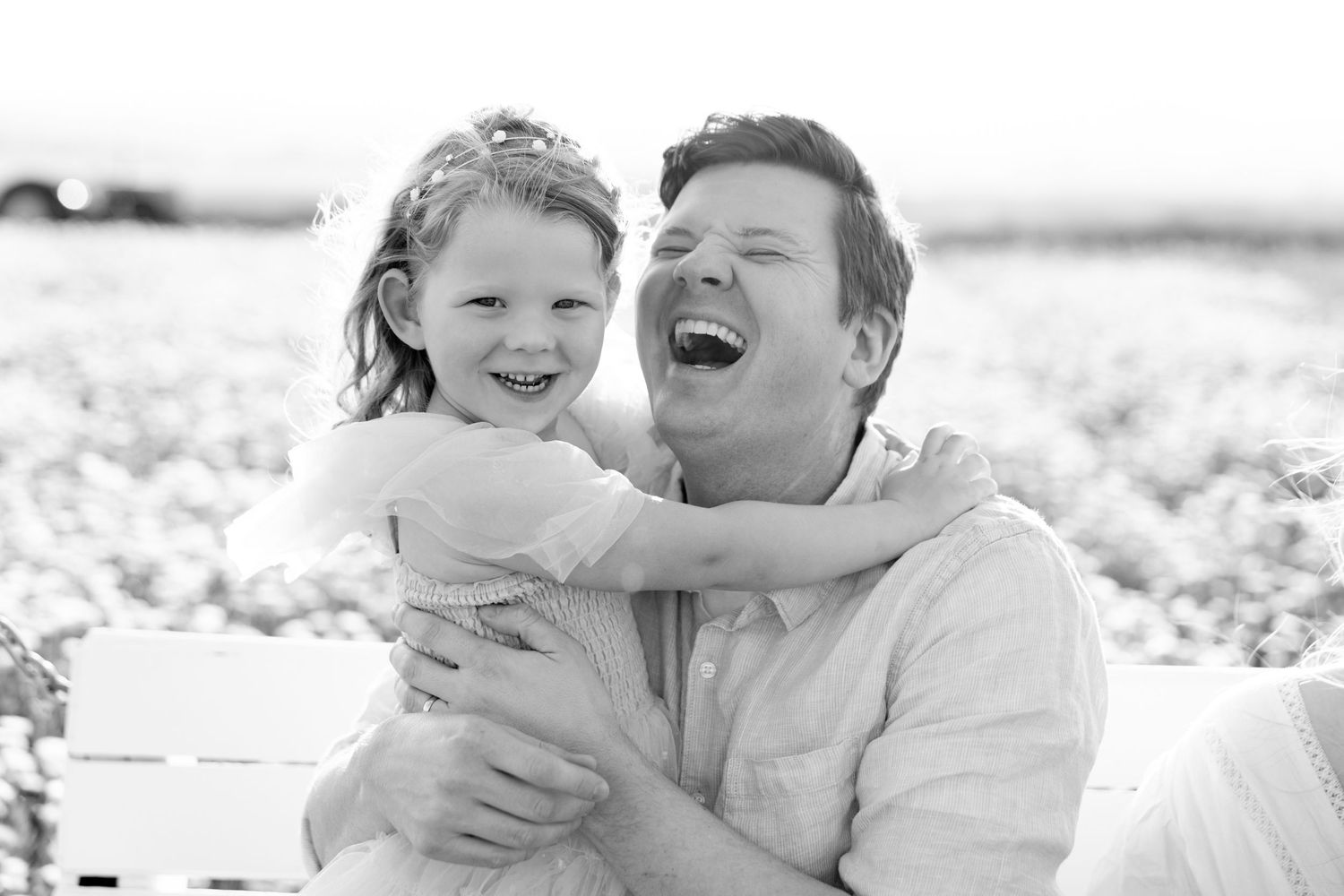 A man and young girl laugh joyfully together in a black and white outdoor portrait photo.