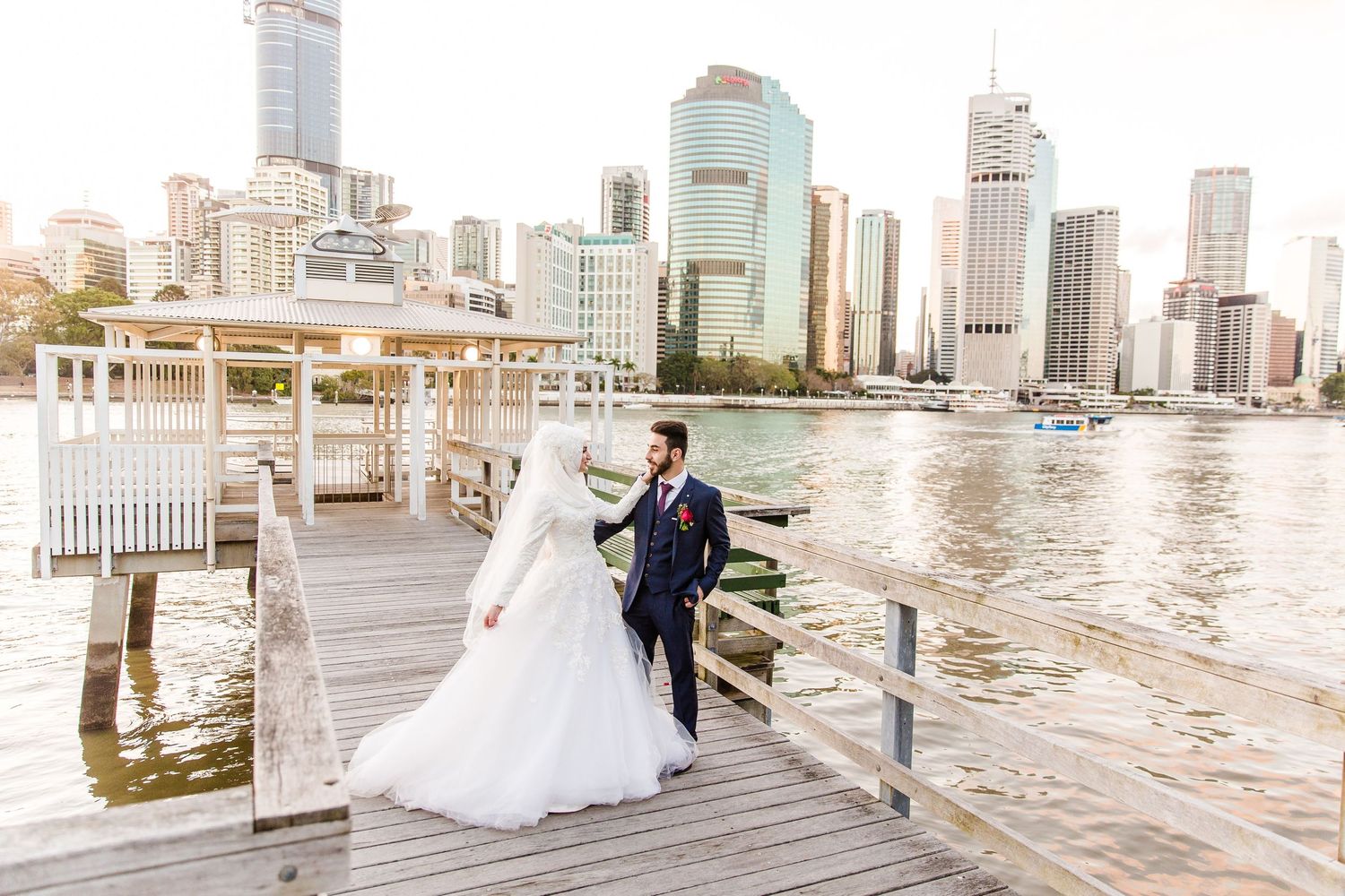 A panoramic view of a wooden pier along the Brisbane River with the city skyline and Story Bridge in the background.
