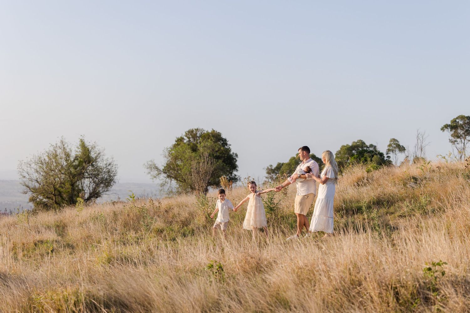 People in white clothing walk together along a scenic hilltop path during golden hour.
