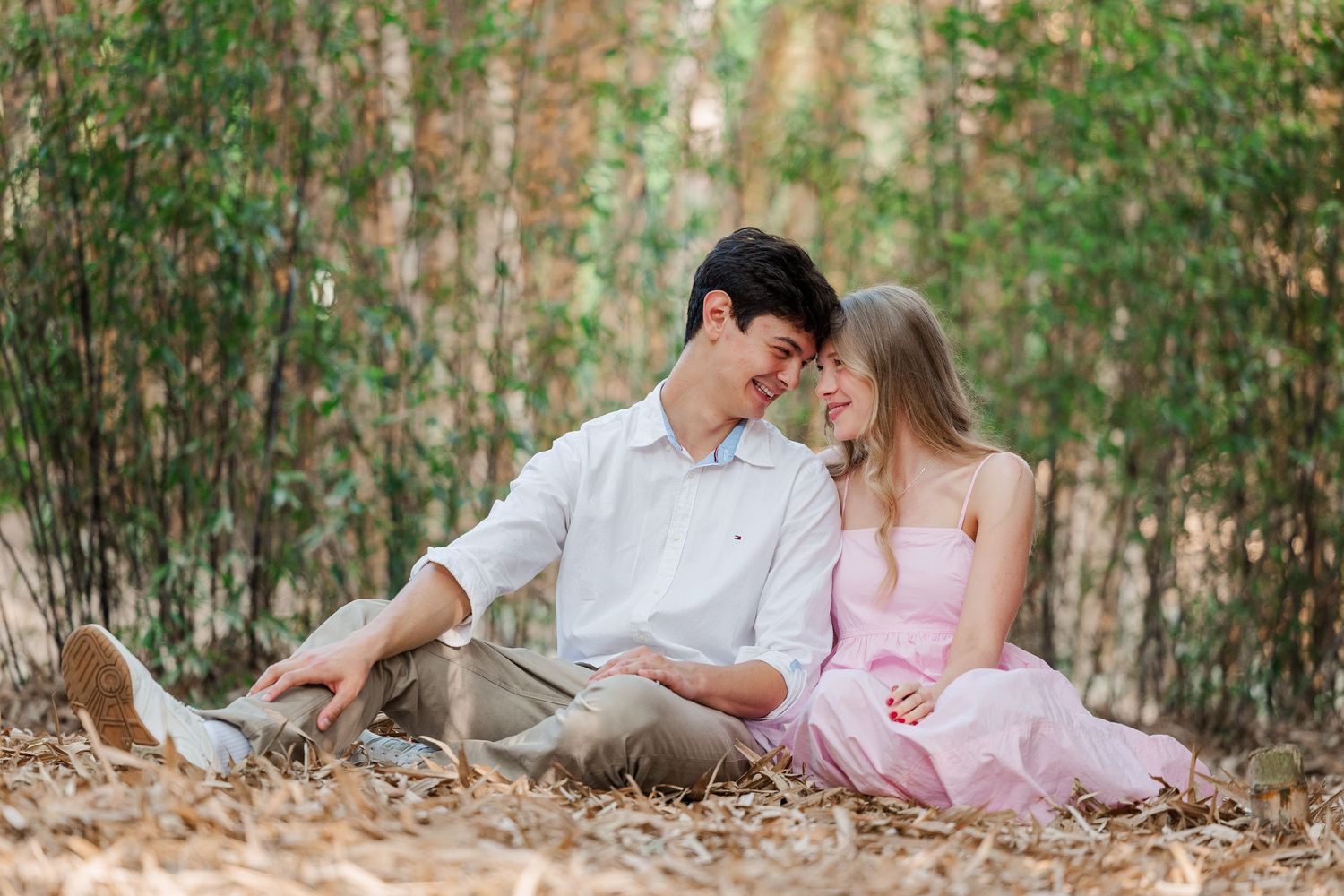 Romantic couple in white and pink outfits share tender moments in a lush bamboo forest setting.