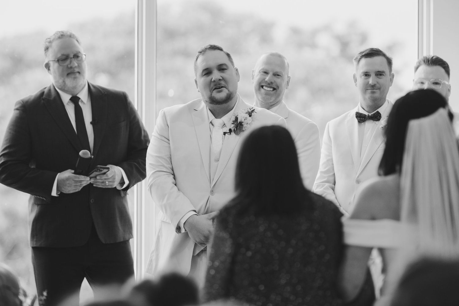 Groom smiling during wedding ceremony with groomsmen in suits and bow ties standing at the altar.