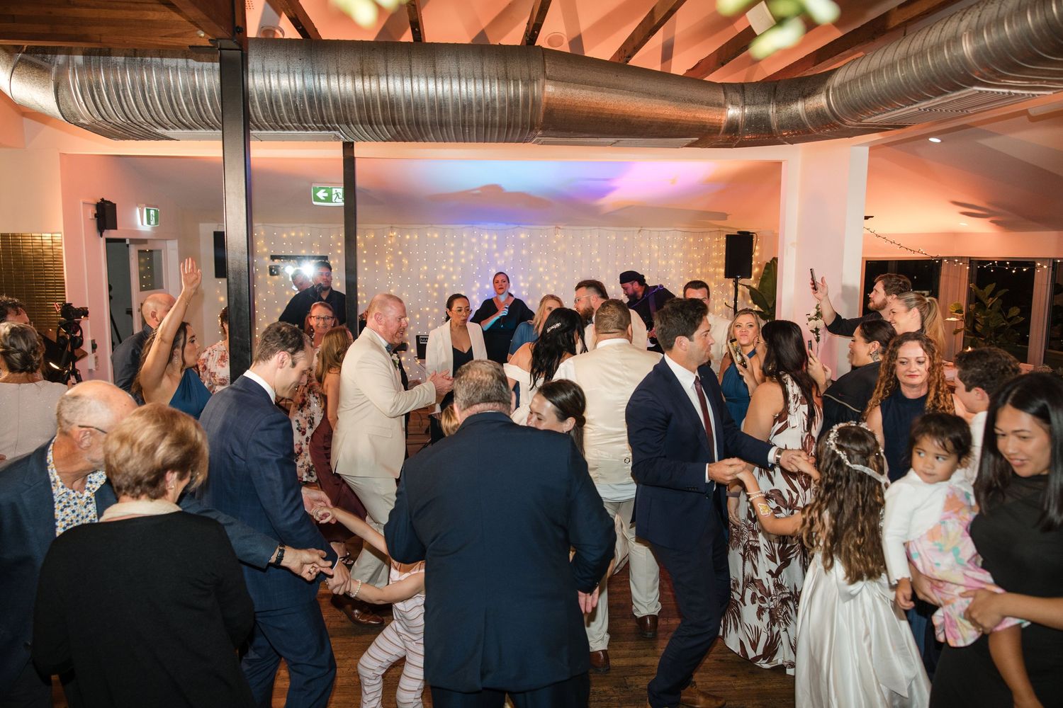 Guests dancing and celebrating at a lively wedding reception in a warmly lit venue.