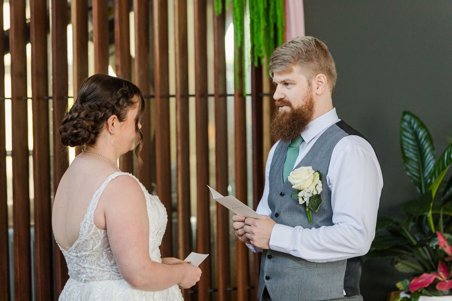 Bride and groom exchanging wedding vows at altar, groom with red beard wearing gray vest with white boutonniere.