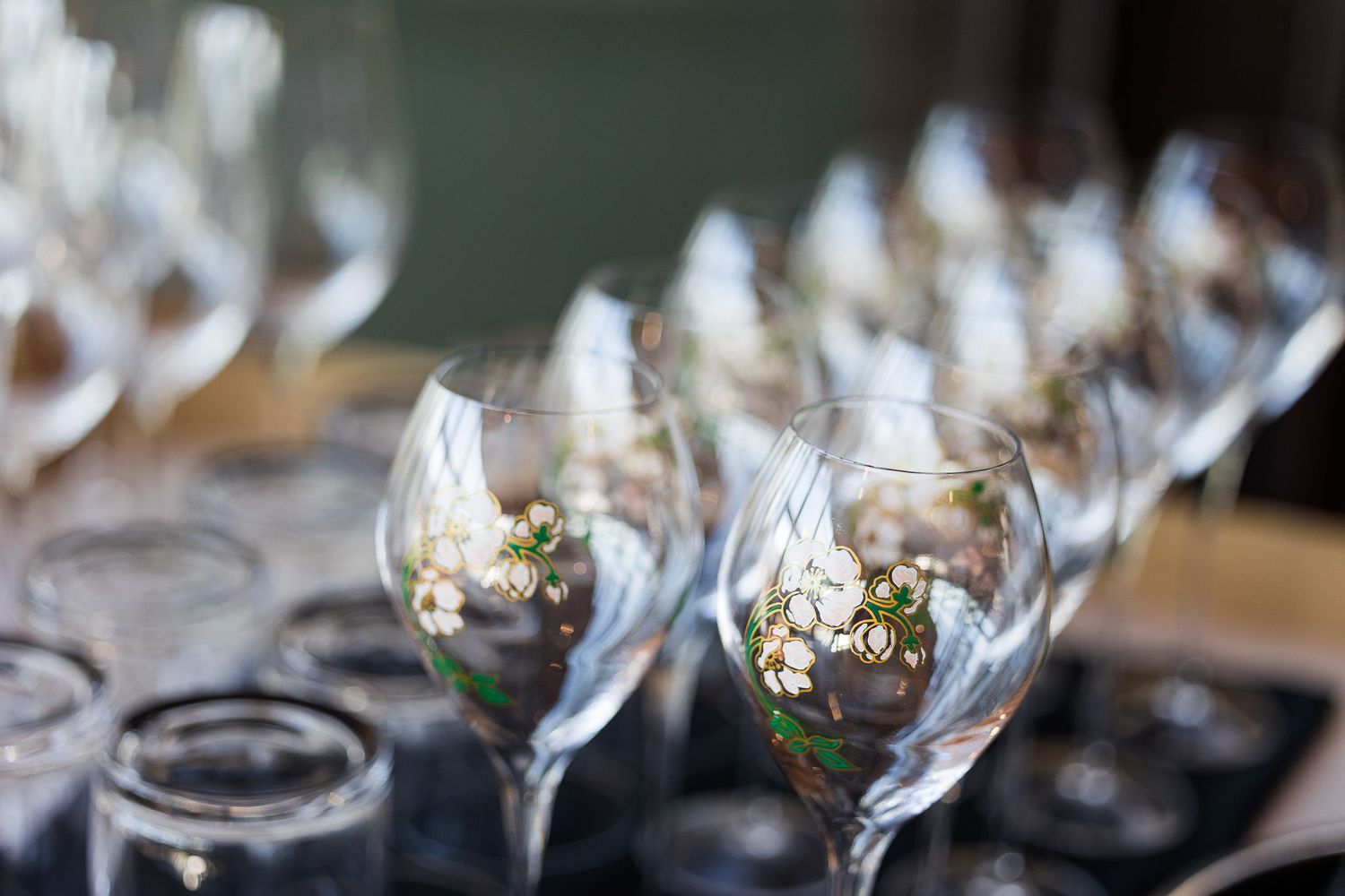 Elegant wine glasses with floral decorations arranged in rows on a dark surface for a wedding reception.