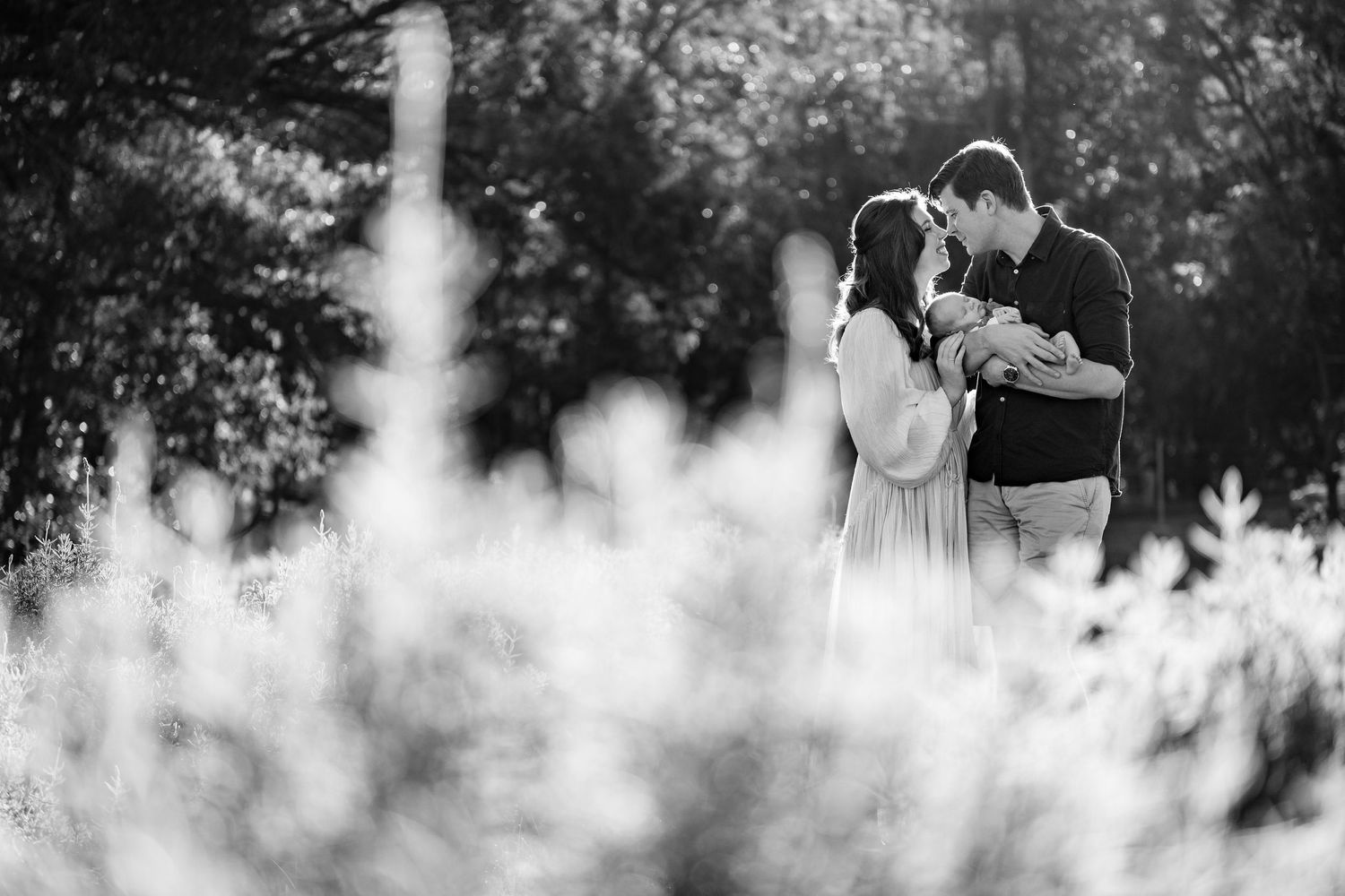 A romantic black and white wedding photo captures an intimate moment between a couple surrounded by dreamy foliage.