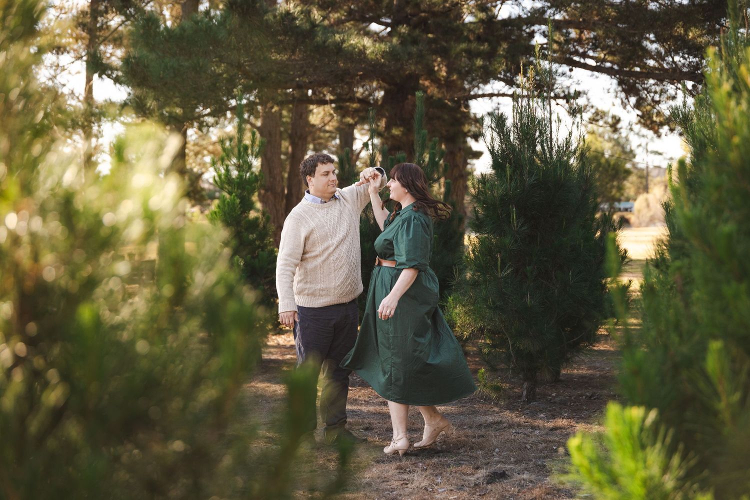 A couple strolls through a serene pine forest path during golden hour as sunlight filters through the trees.