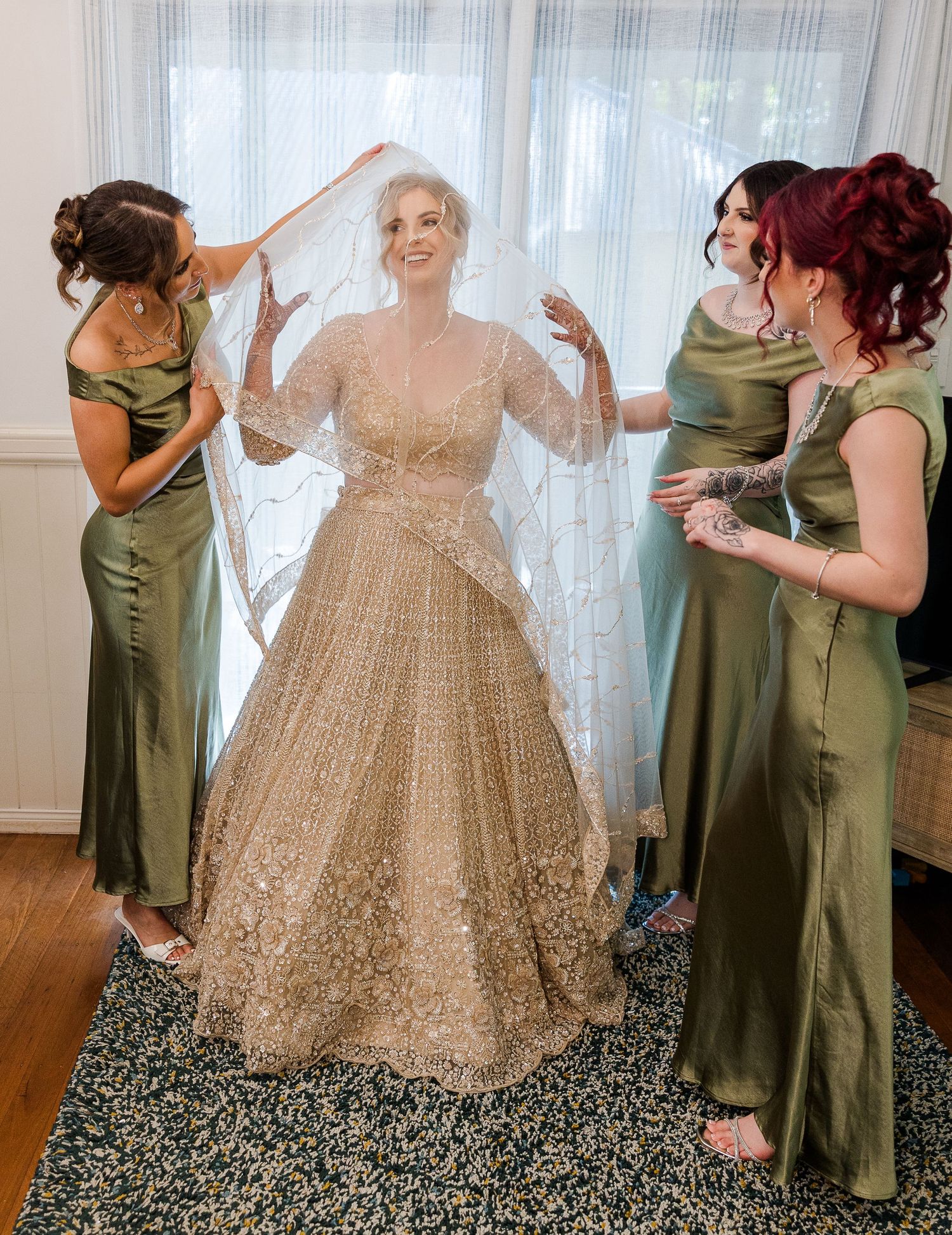 Bride in gold embroidered gown with veil, assisted by three bridesmaids in olive green dresses.