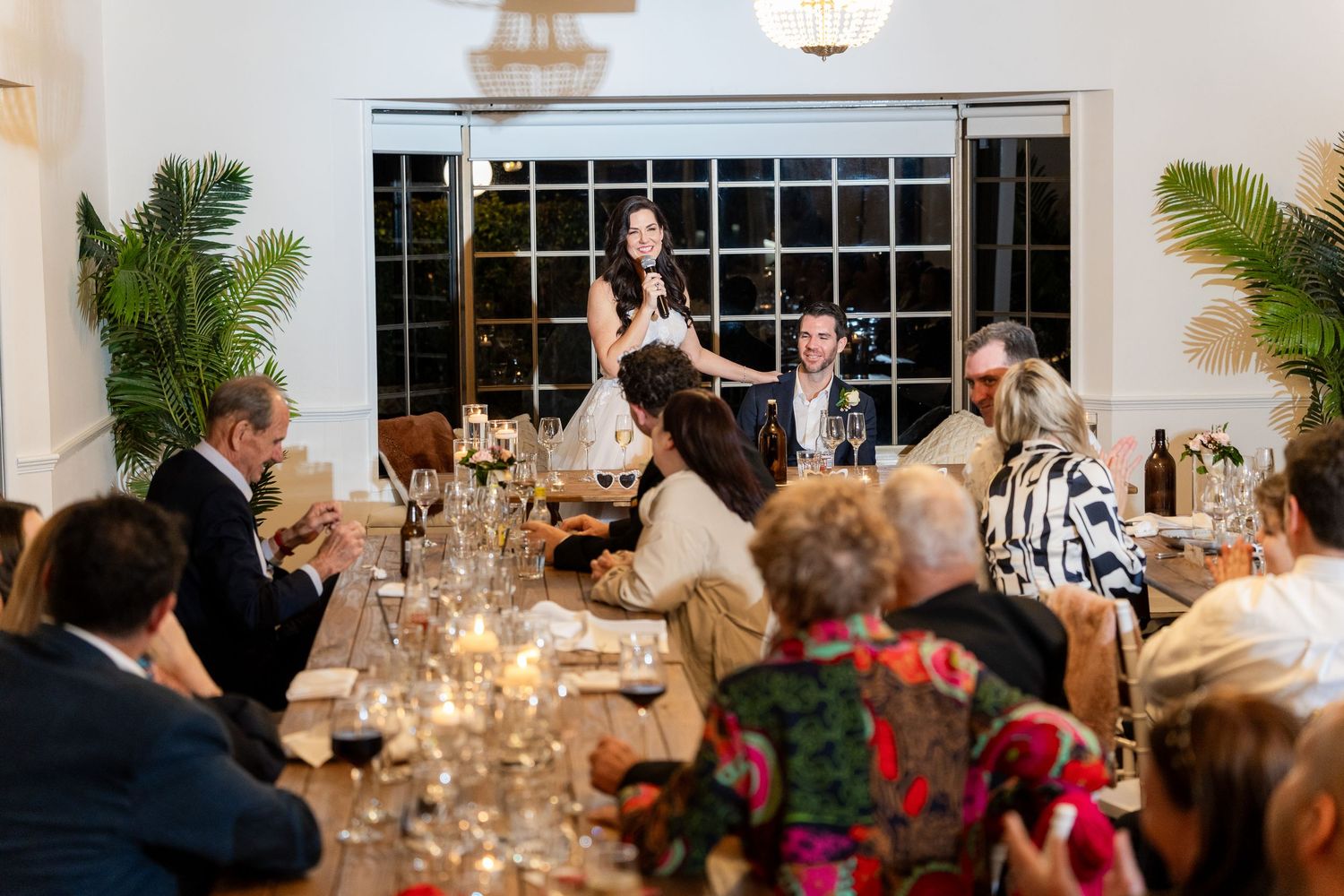 Wedding guests enjoying an elegant dinner reception at long tables decorated with candlelight and floral arrangements.