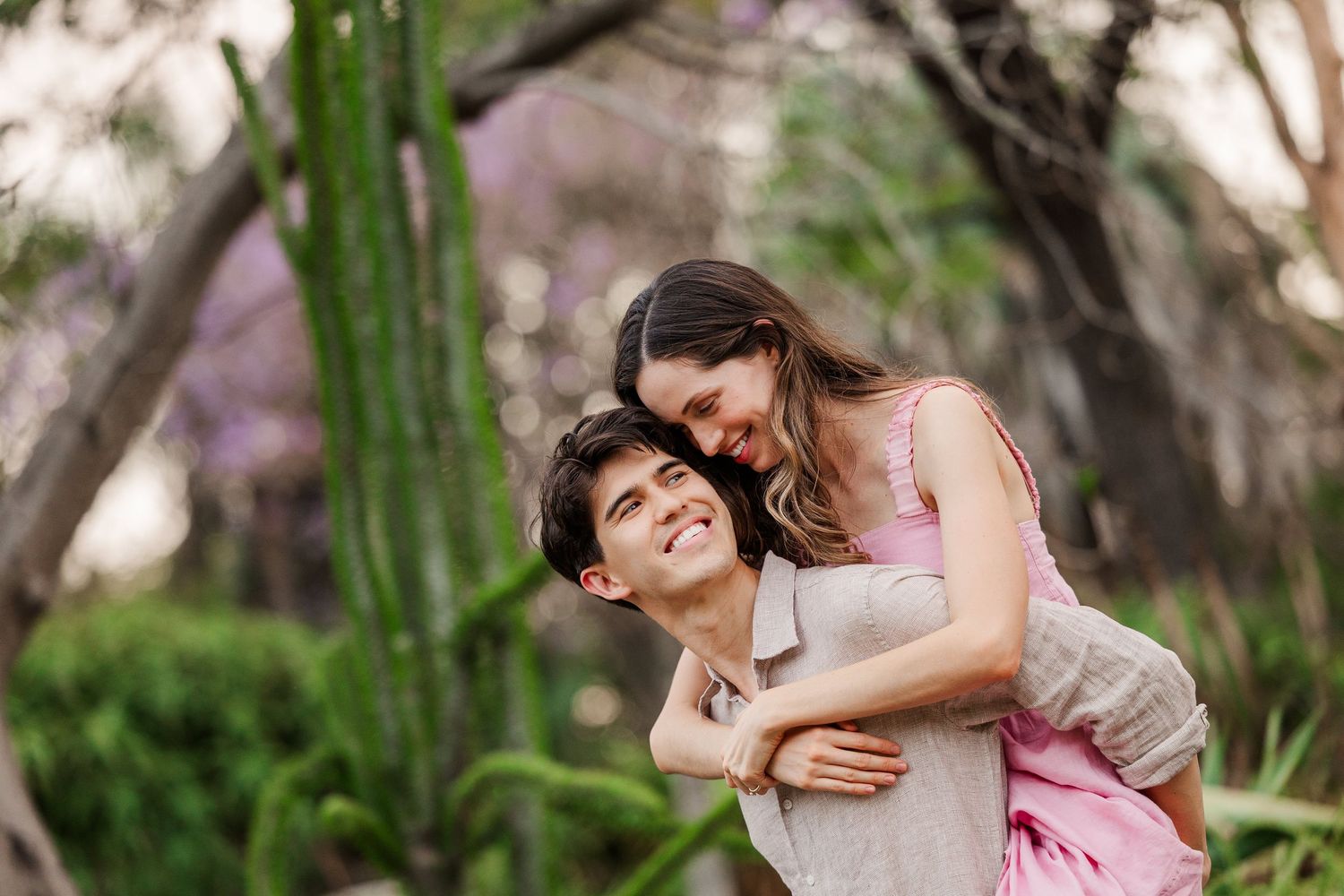 Two people in pink dresses share joyful moments together in a sunlit garden setting.