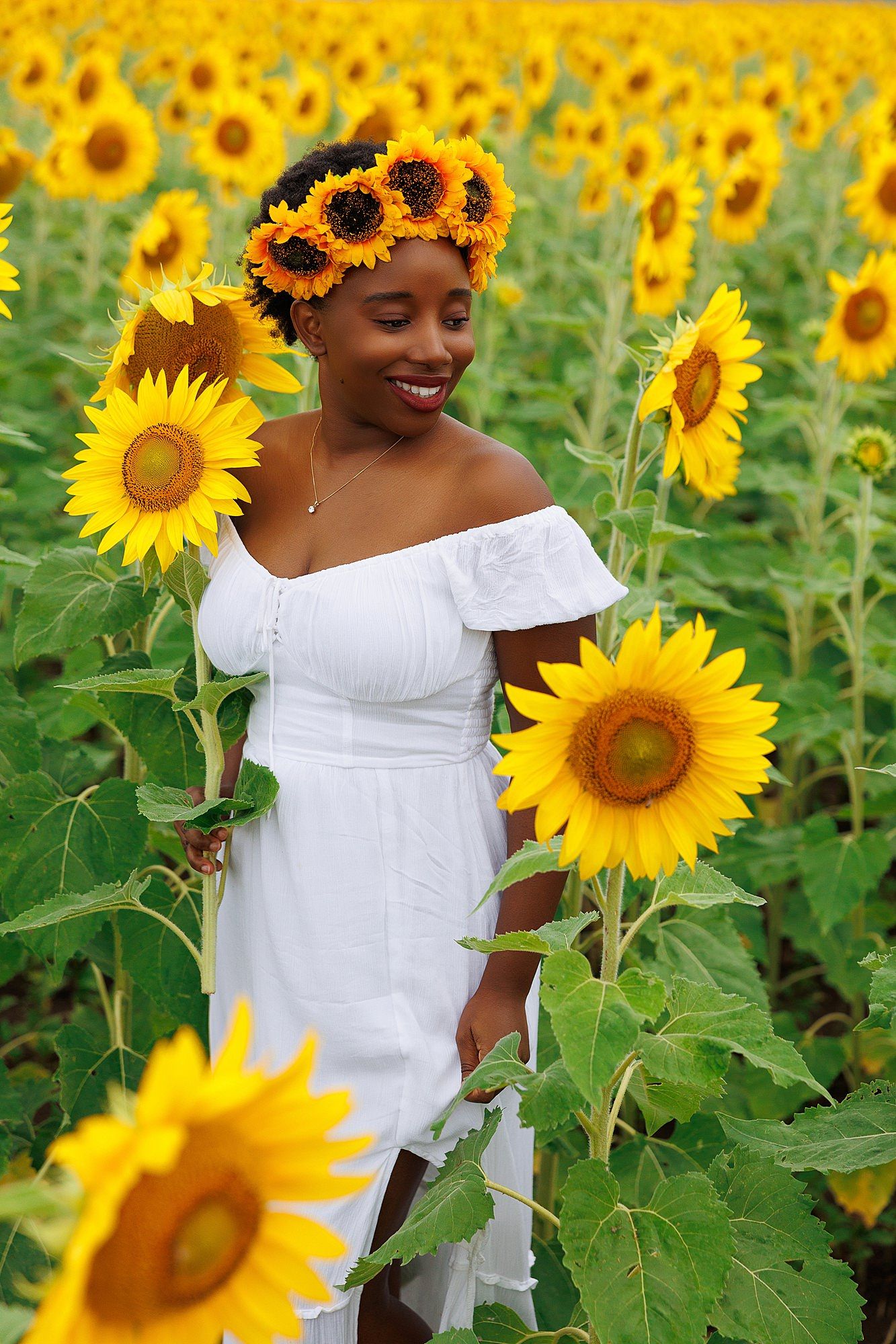 Beautiful summer scene in a sunflower field with a flowing white dress and floral crown surrounded by vibrant blooms.