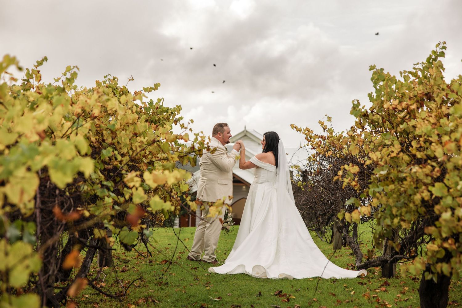 Bride and groom share vows among lush vineyard rows under dramatic cloudy skies at an outdoor winery wedding.