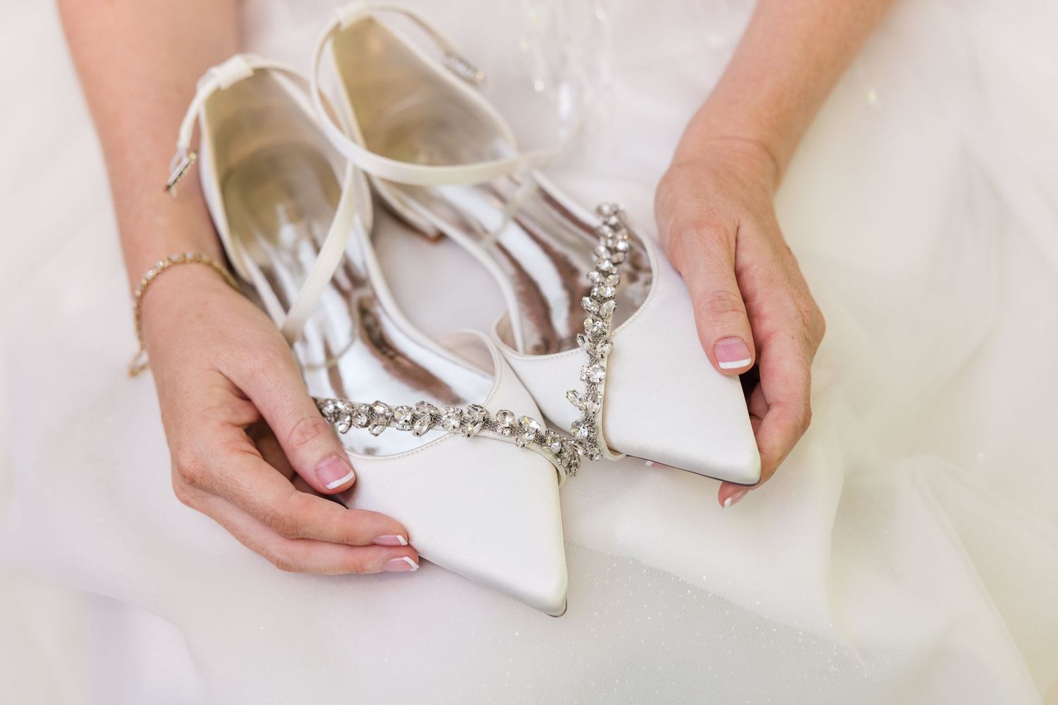 Hands carefully tying a white satin bow on an elegant bridal gown or formal dress.