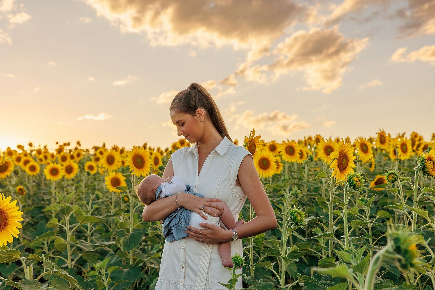 Person in white dress stands among tall sunflowers during golden sunset.