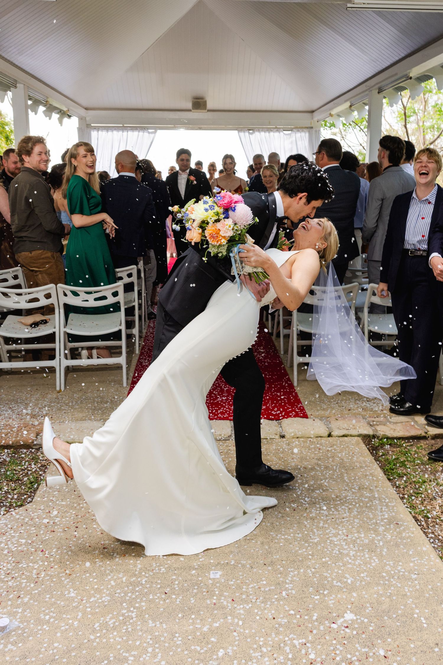 Wedding couple dances together during their first dance while guests watch and celebrate at an outdoor reception venue.