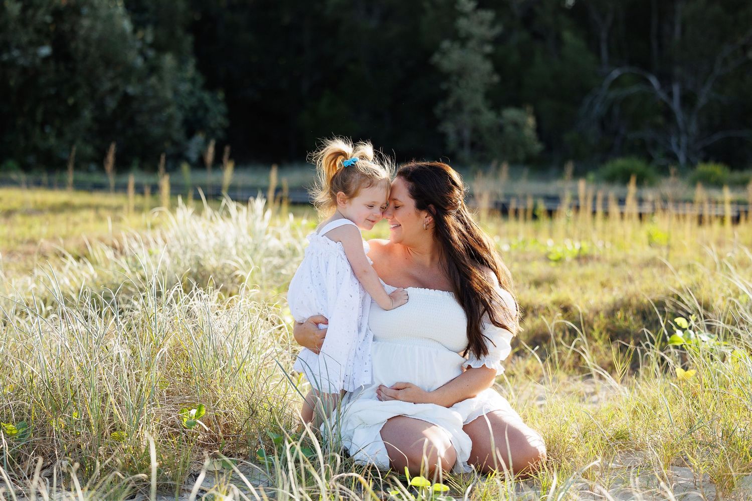 A tender moment shared in a sunlit meadow with tall grass and wildflowers in the golden afternoon light.