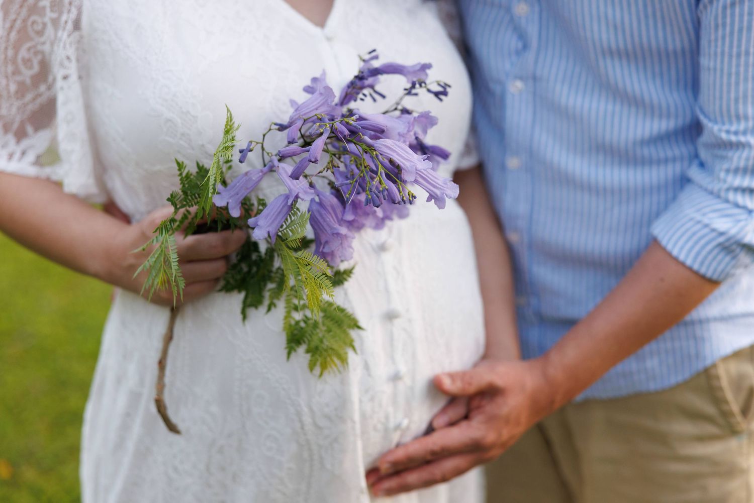 A couple holds purple floral bouquets while wearing blue and white attire at an outdoor wedding ceremony.