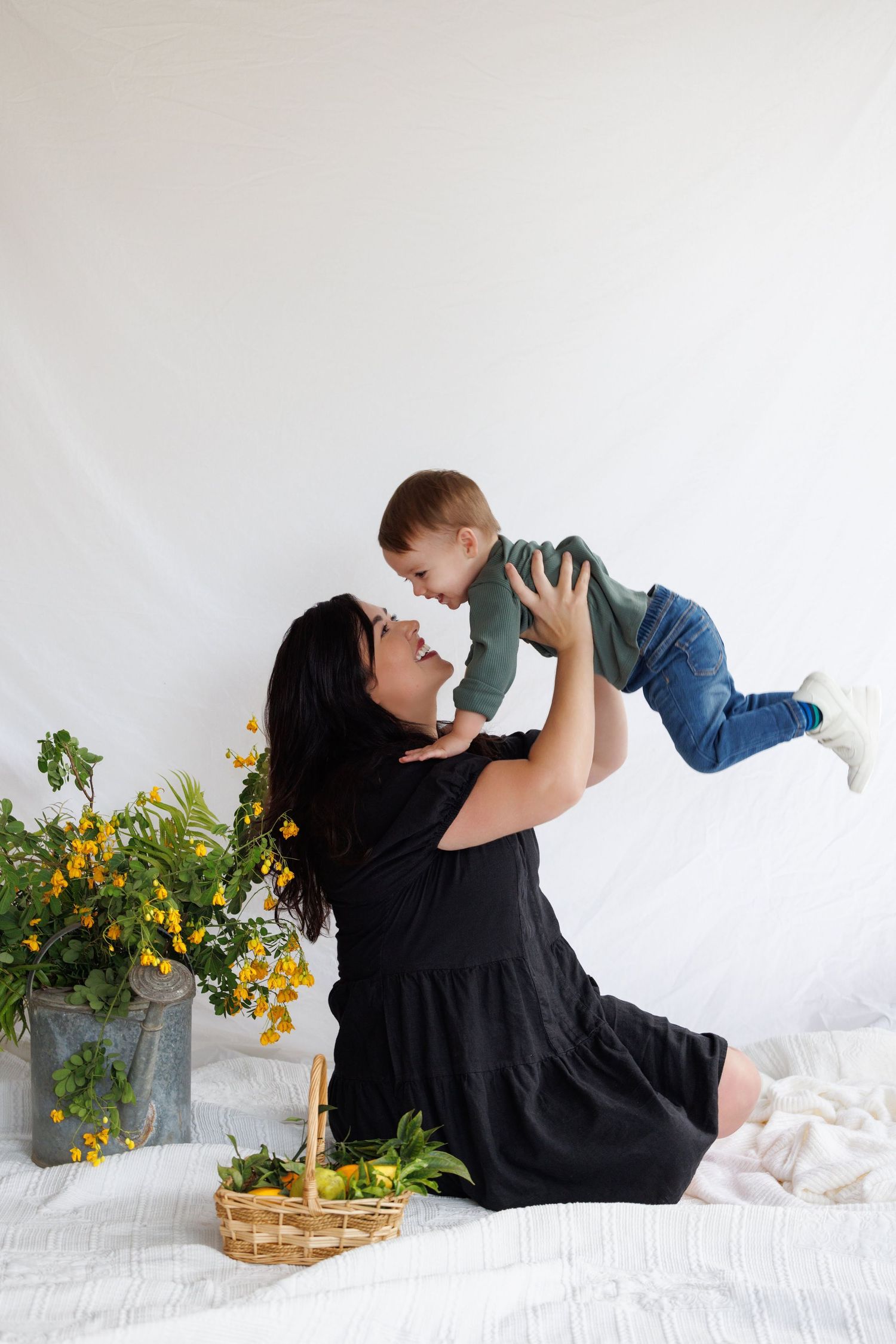 Parent and child in black shirts lying on white bedding with yellow flowers displayed in metal container beside them.