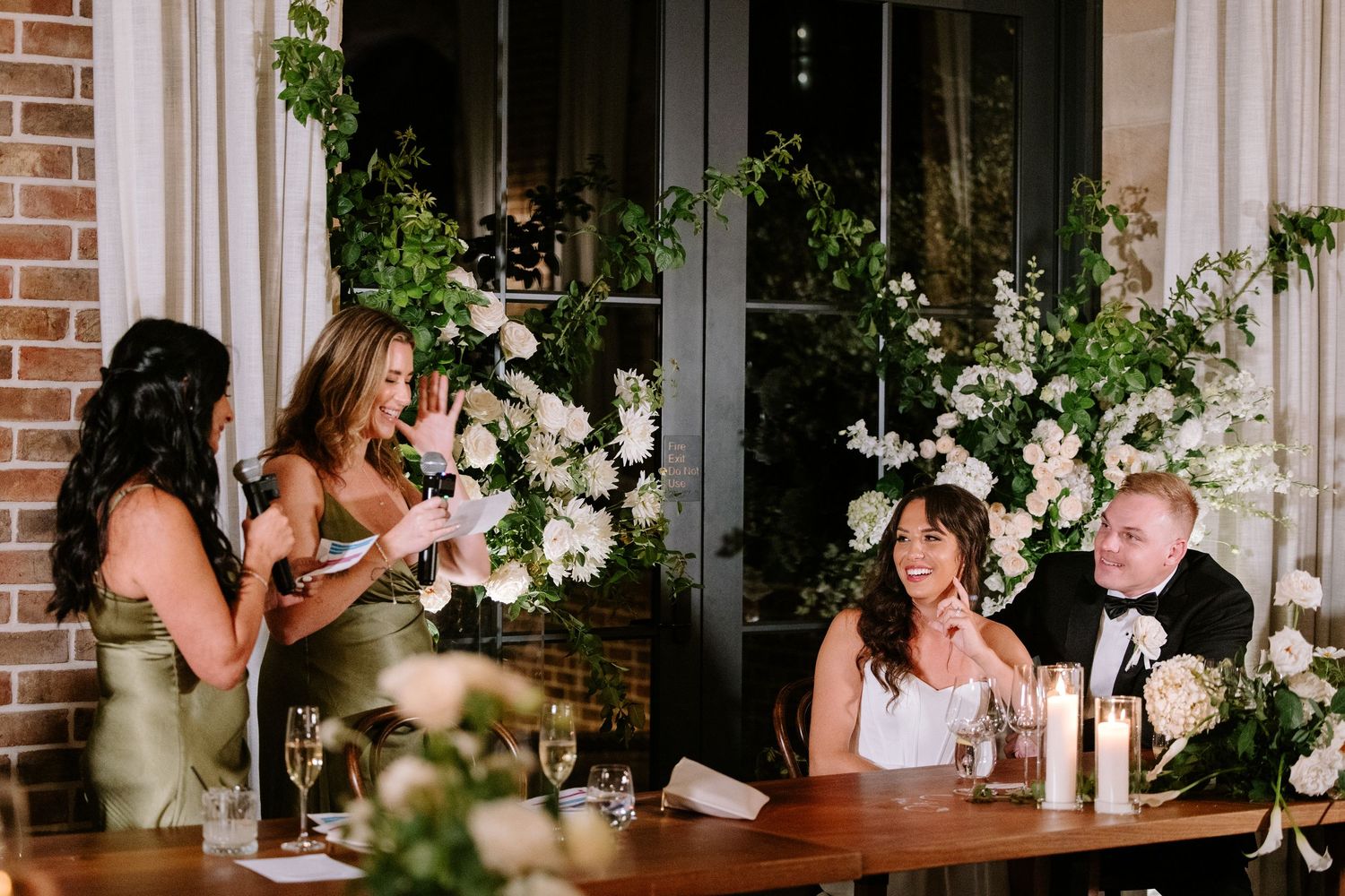 Wedding reception guests share laughter and conversation at an elegant dining table decorated with floral arrangements.
