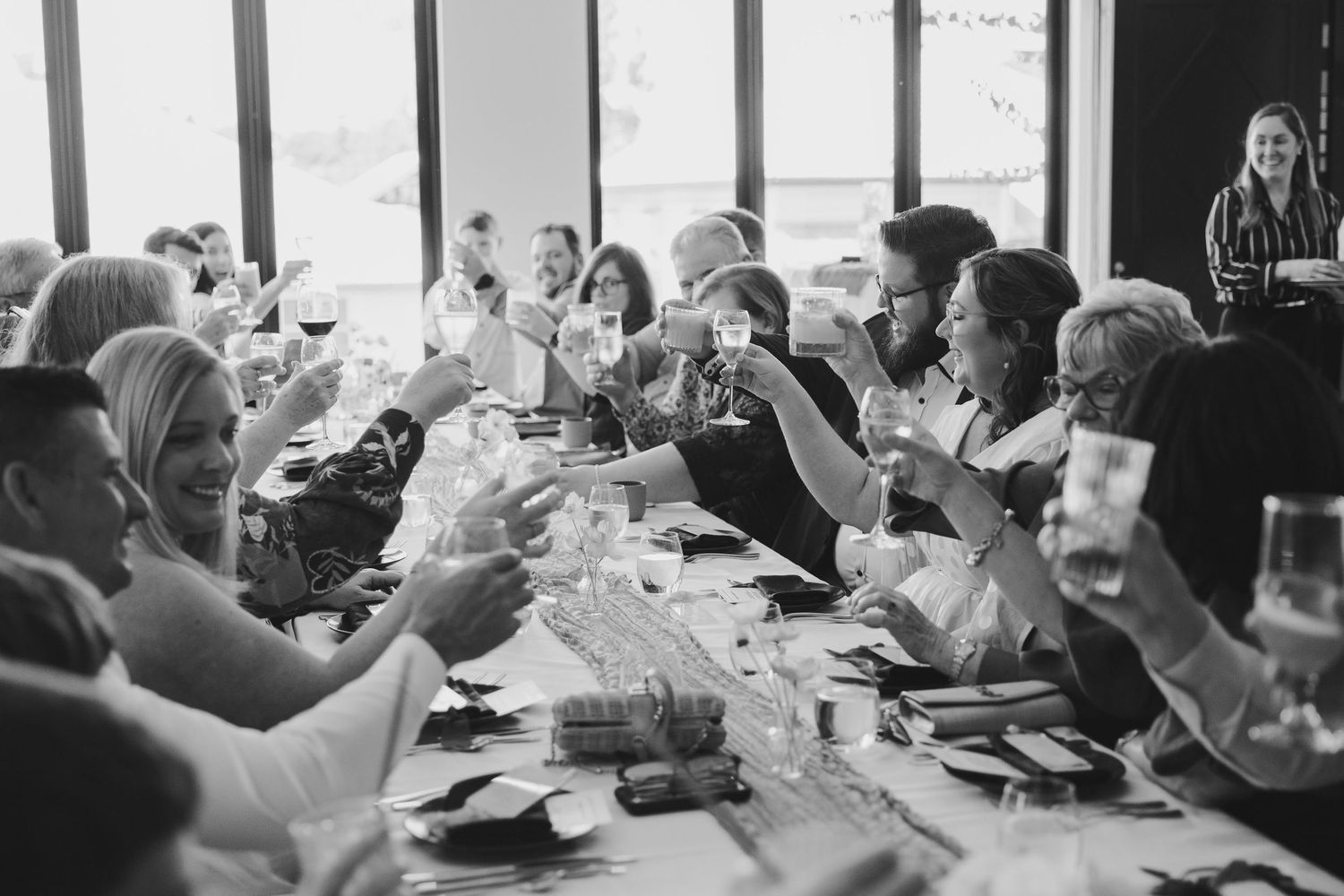 Black and white photo of people gathered around tables at a social dining event in a restaurant setting.