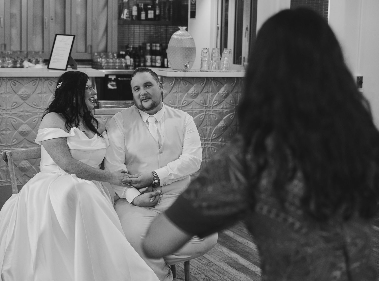 Black and white photo of a bride and groom sitting together at their wedding reception, smiling warmly.