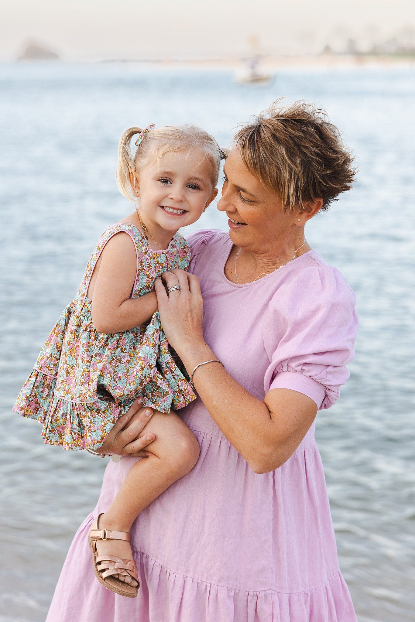 Two people in pink dresses sharing a tender moment by the water during sunset.
