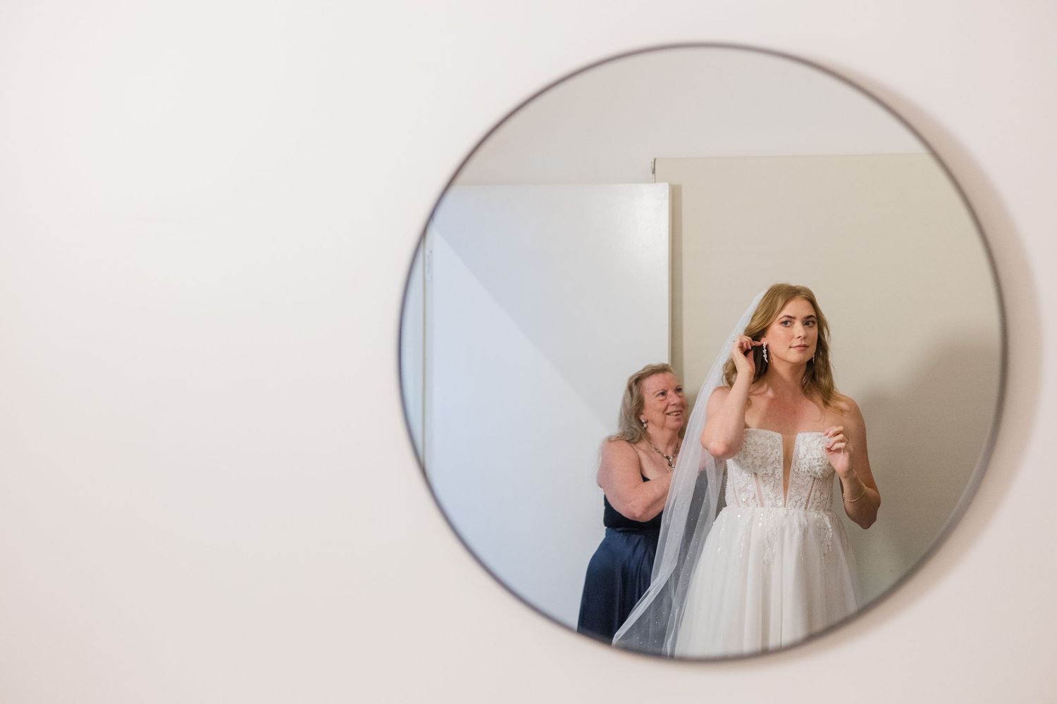 A series of oval mirrors mounted on a wall reflect wedding dress preparations in an elegant setting.