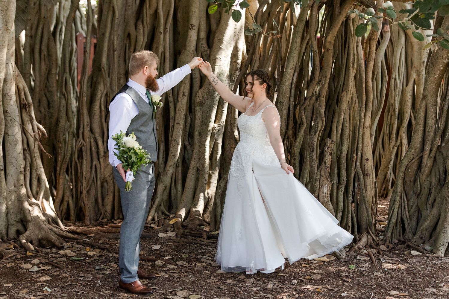 Bride and groom dancing together under sprawling banyan tree roots during outdoor wedding photo session.