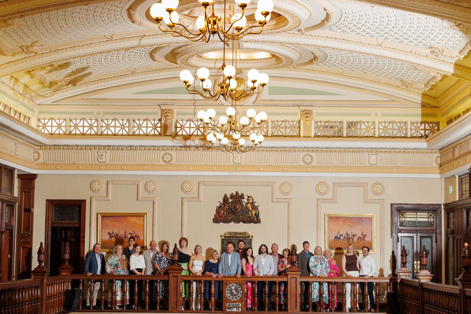 A grand historic courtroom with ornate ceiling, crystal chandeliers and wooden furnishings filled with spectators.