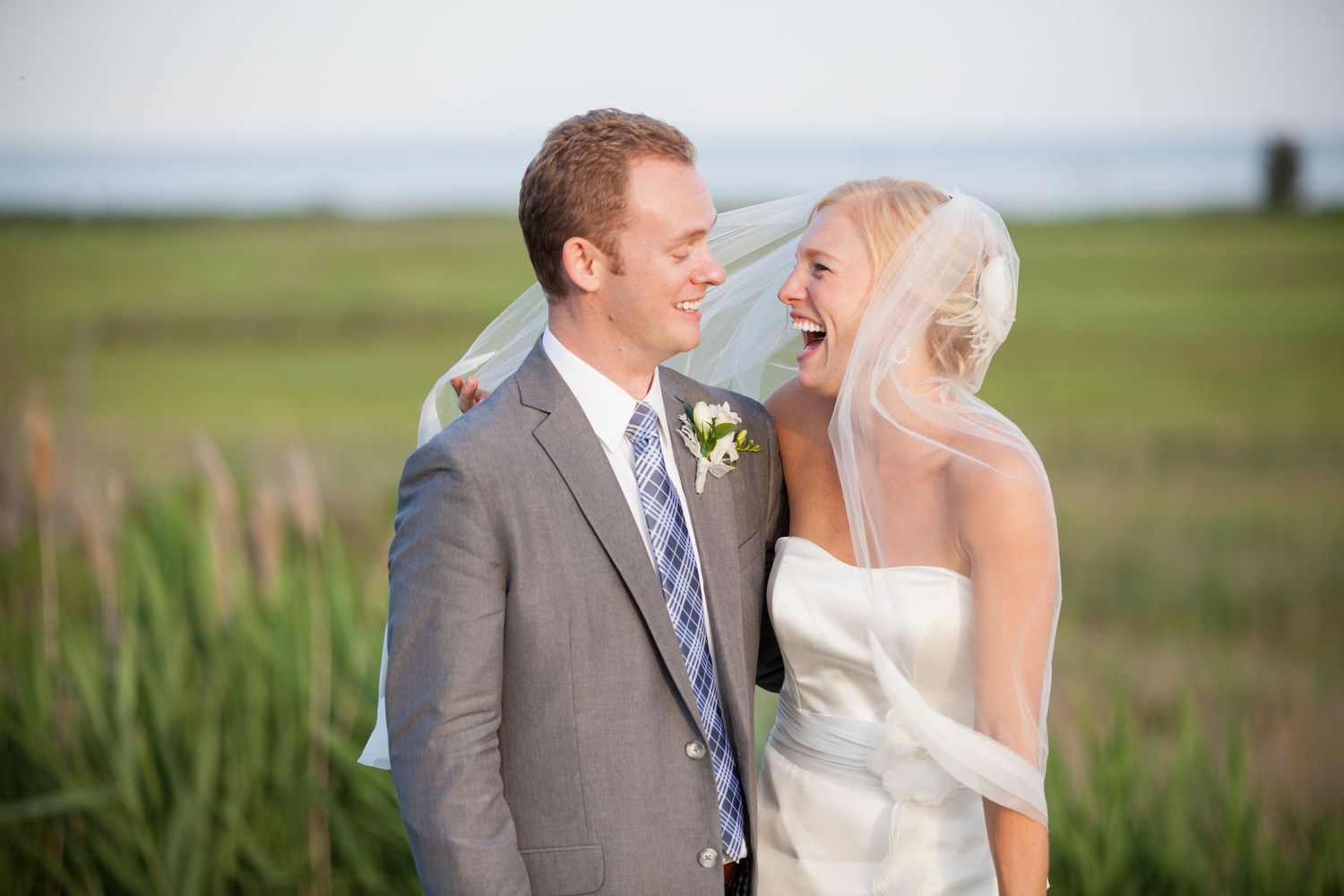 A couple shares a romantic moment in a grassy field wearing wedding attire on their special day.