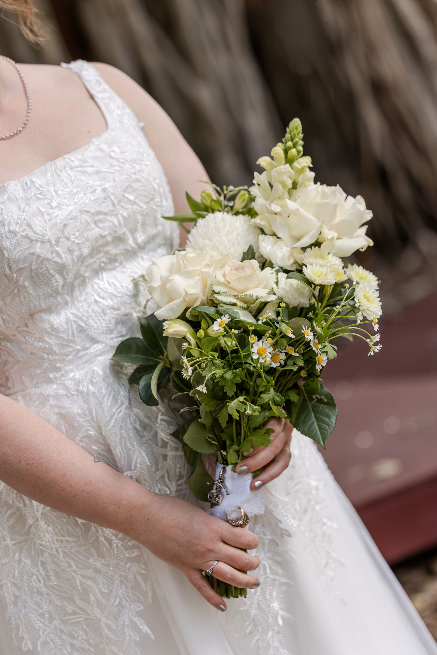 Bride holding elegant white wedding bouquet with roses and greenery, wearing lace bridal gown.