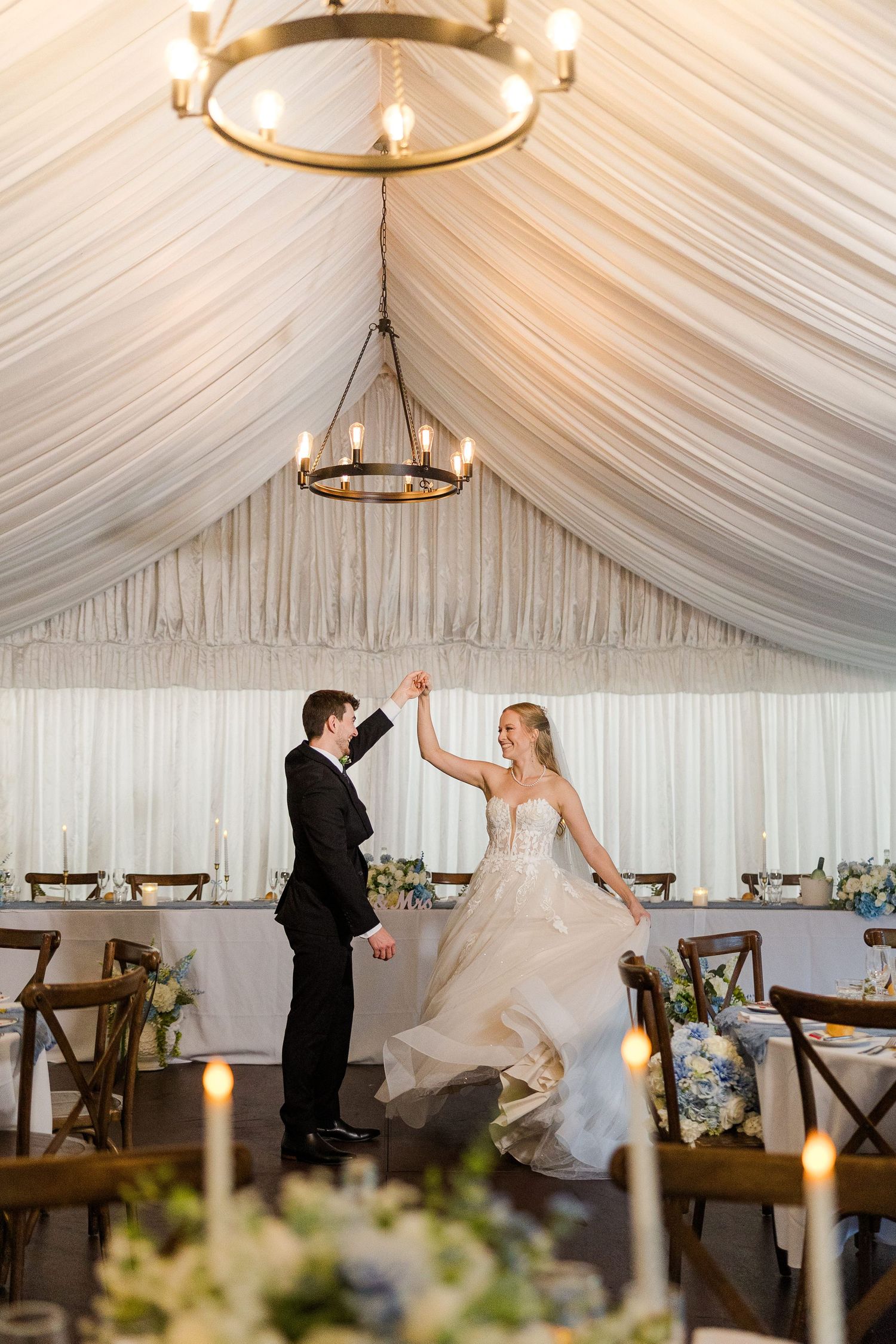 Bride and groom share first dance under elegant draped tent ceiling with chandelier at romantic candlelit wedding reception.