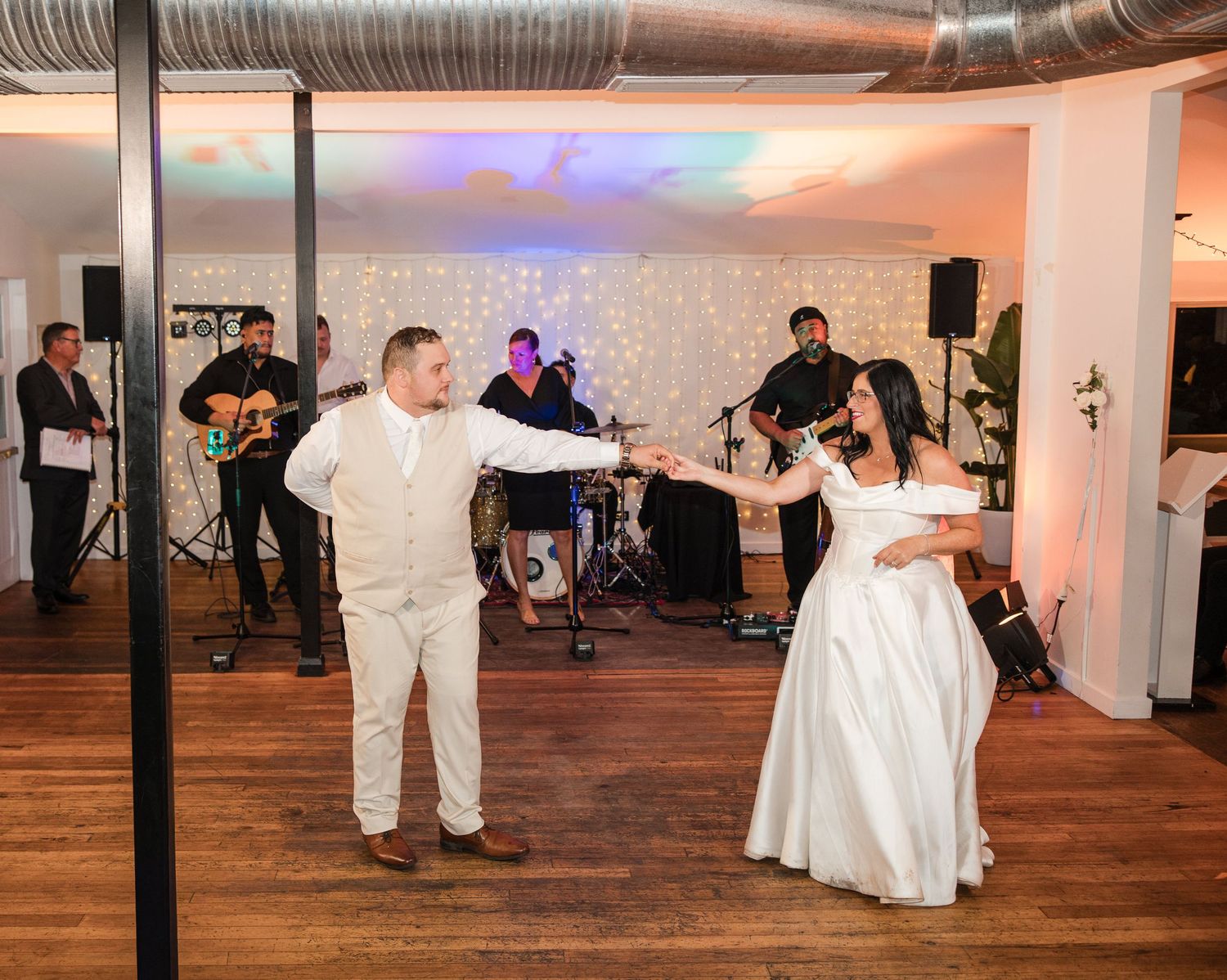 Bride and groom share first dance at wedding reception with live band performing in background.