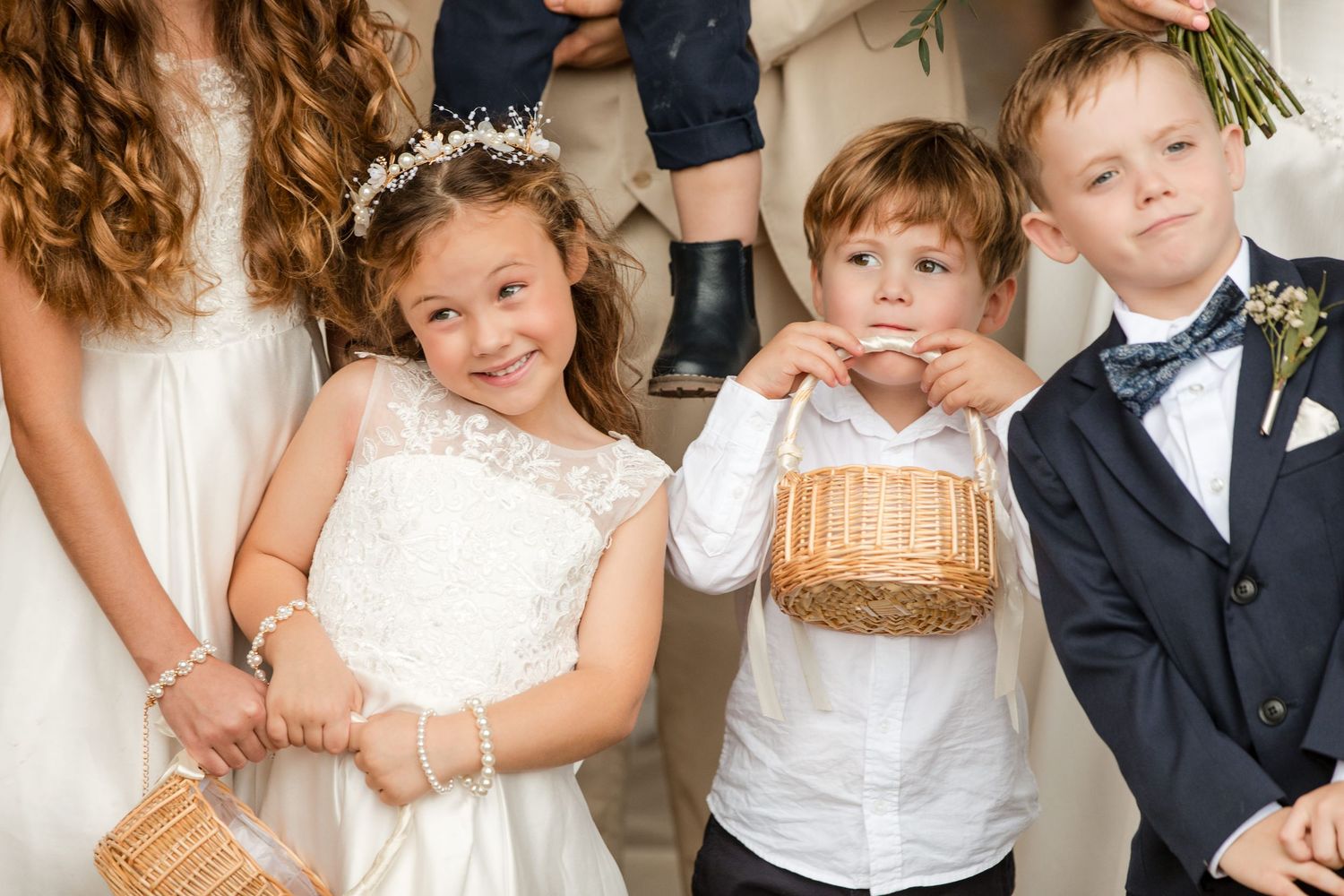 Two flower girls in white dresses and two ring bearers in suits pose together at a wedding ceremony.