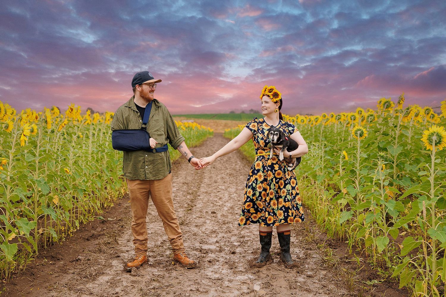 Two people dancing along a dirt path between tall blooming sunflower fields during a vibrant sunset.