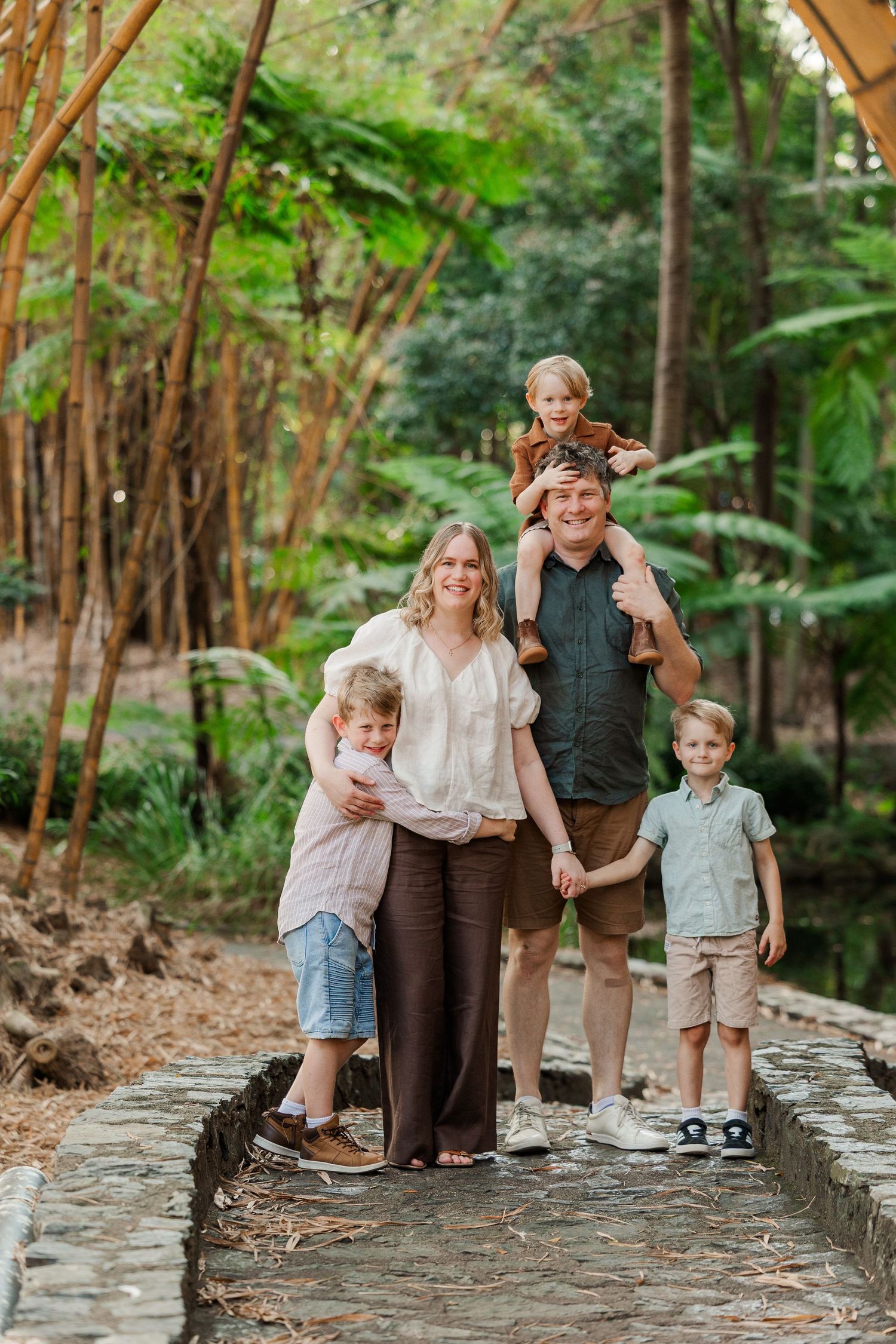 Family walking and playing together on a stone wall path surrounded by bamboo trees in a garden setting.