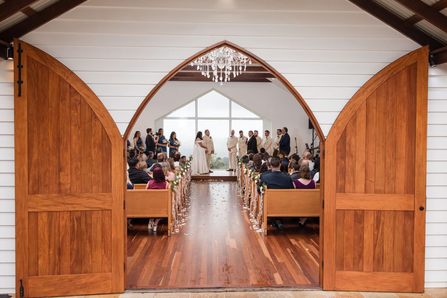 Wooden chapel doors open to reveal a wedding ceremony with guests seated in pews and couple at the altar.