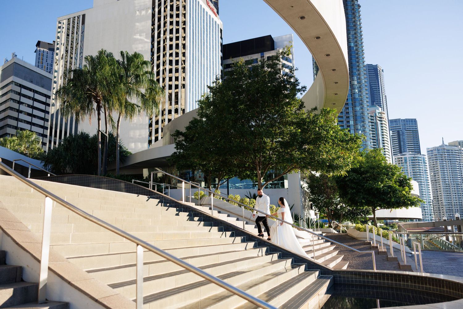 A skateboarder performs a trick down a curved concrete stairway with urban buildings visible in the background.