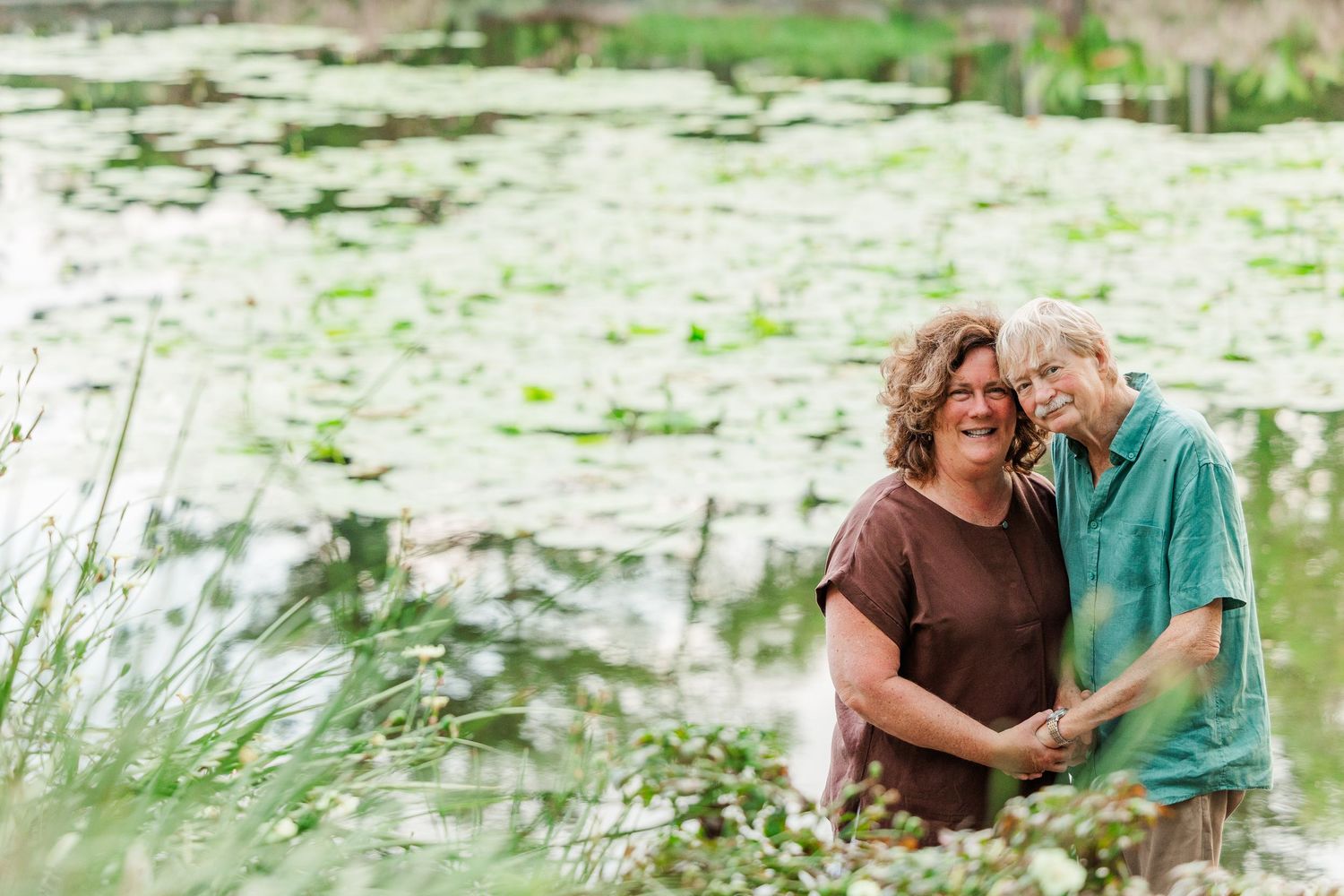 Family photoshoot by a serene pond with lily pads and natural greenery in the background.