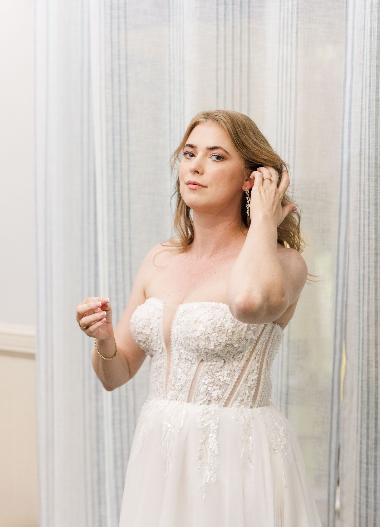 A person in a sheer white lace robe poses gracefully against a light-colored background with vertical curtains.