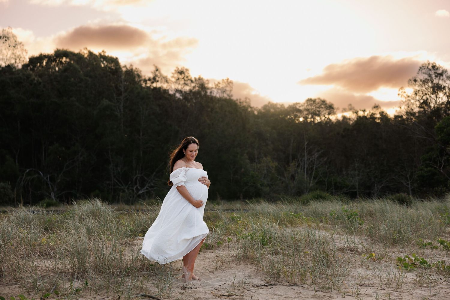 A flowing white dress catches the breeze in a golden field at sunset, creating a dreamy outdoor scene.