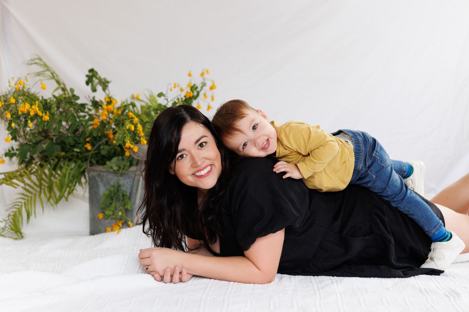 A parent in black dress lying on white floor with yellow flowers in background as decor.