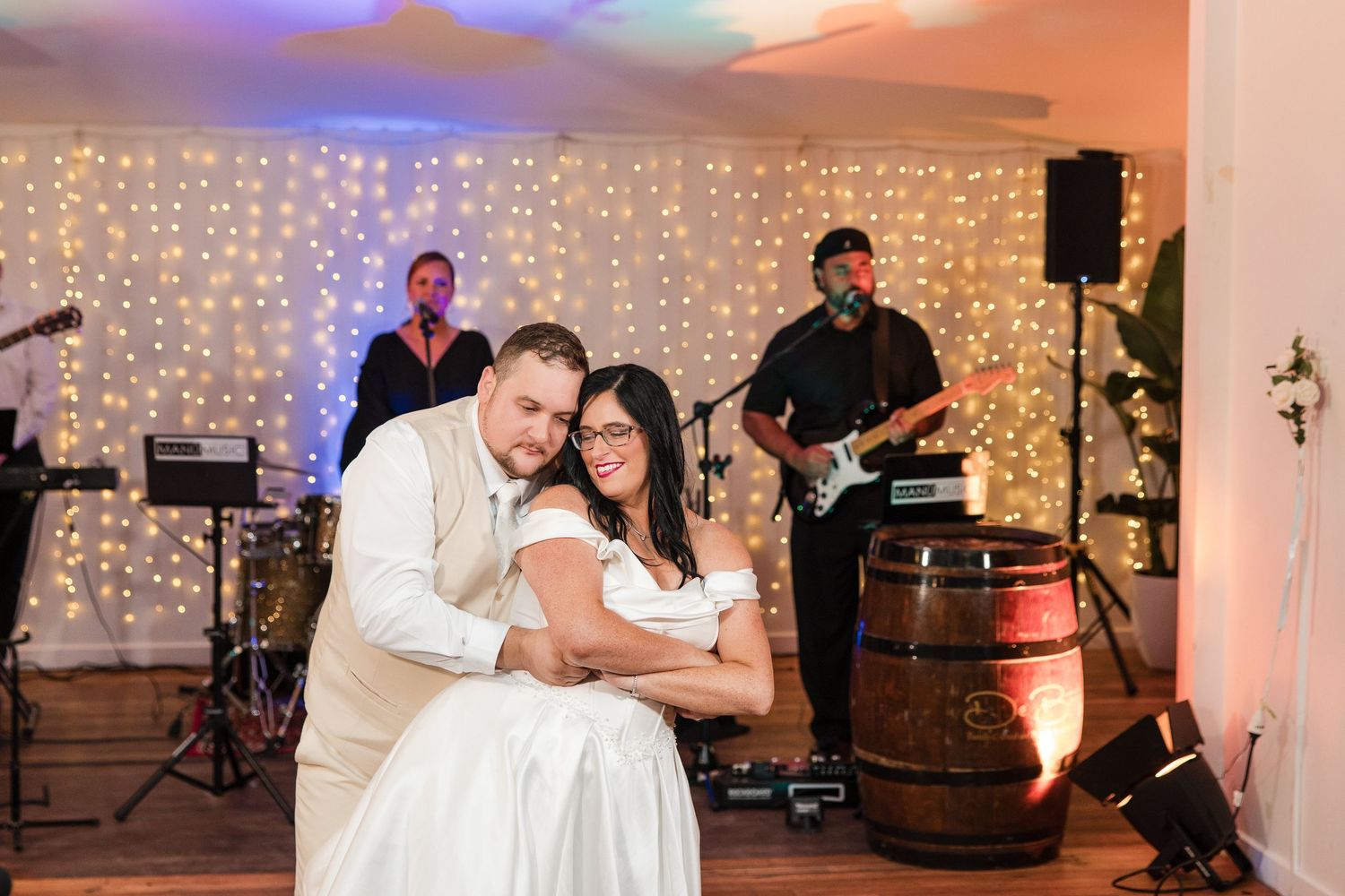 Bride and groom share first dance at wedding reception with live band and fairy lights backdrop.