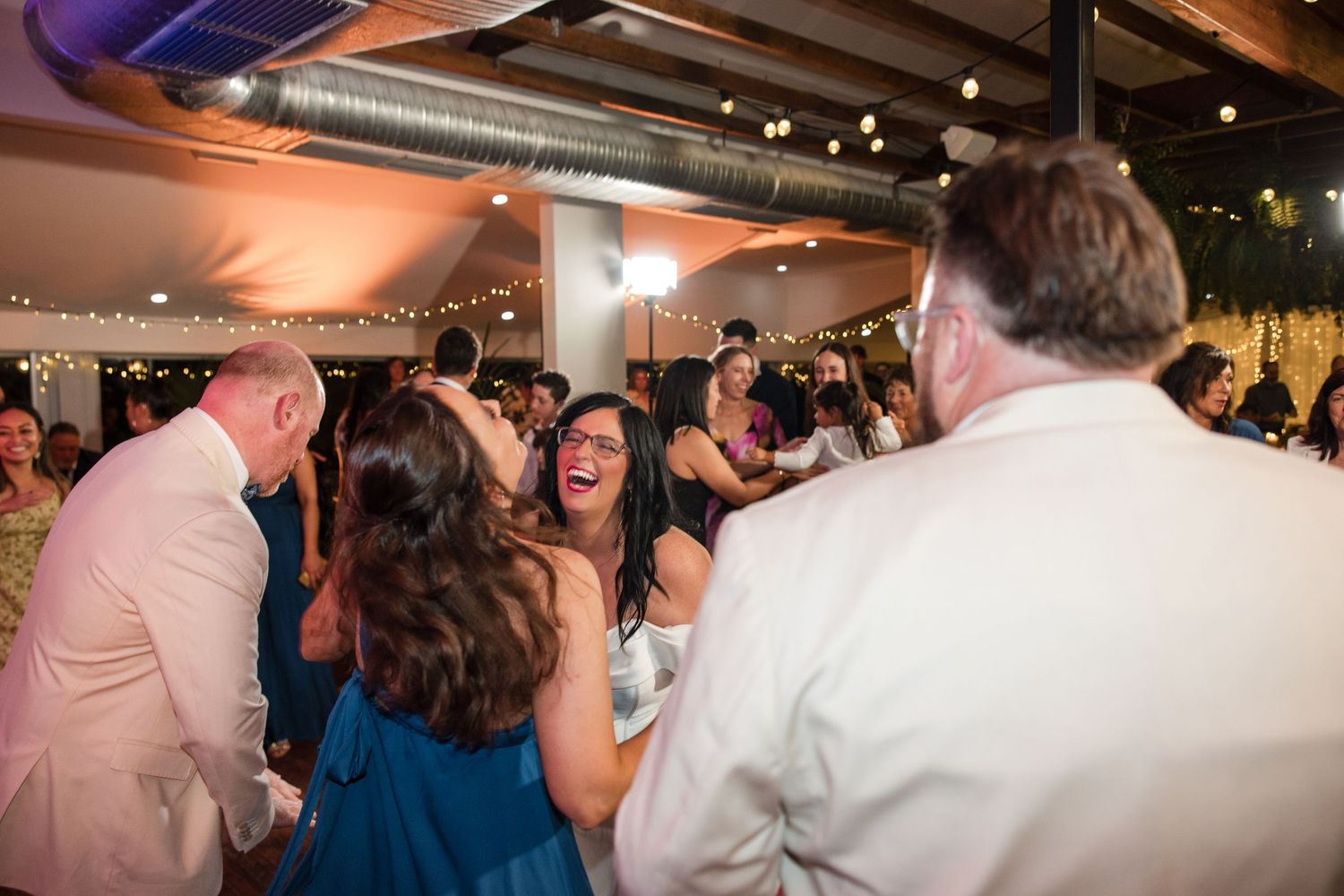 Guests laughing and dancing joyfully at an indoor wedding reception with warm ambient lighting.