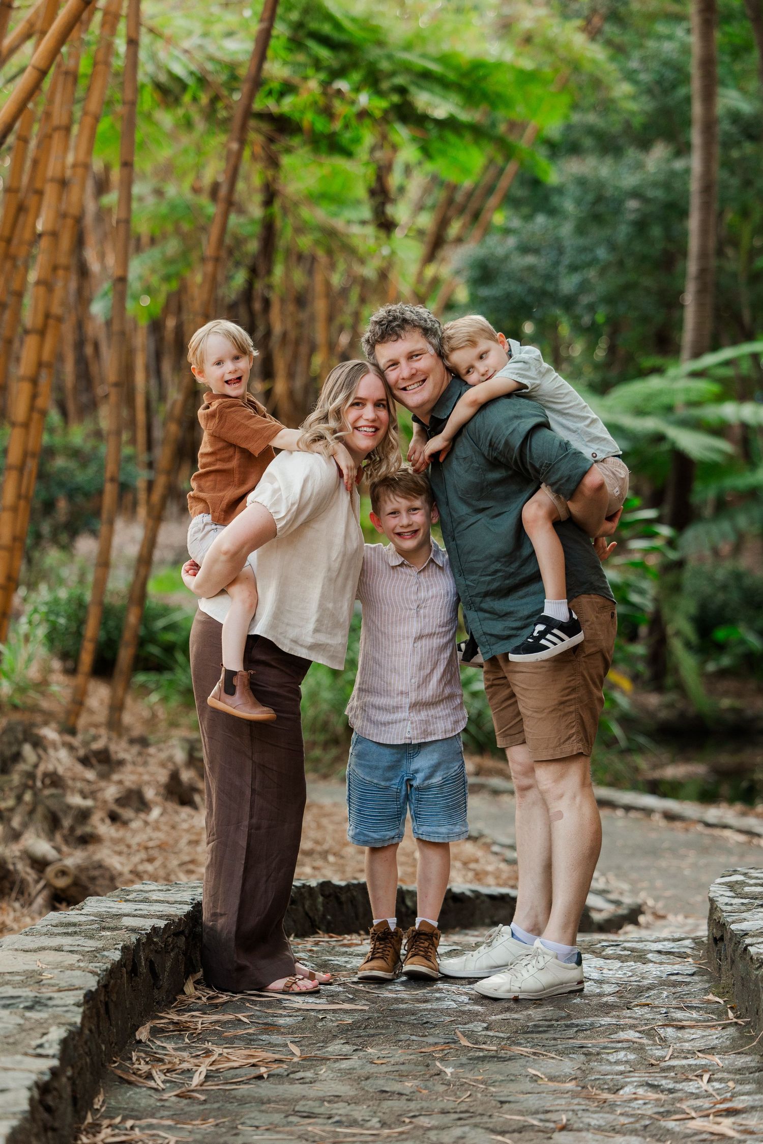 Family enjoying playful moments together on a stone path surrounded by tall redwood trees in a forest setting.