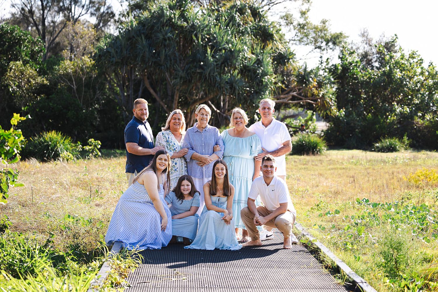 A group poses together on a pathway surrounded by blooming wildflowers and greenery on a sunny day.