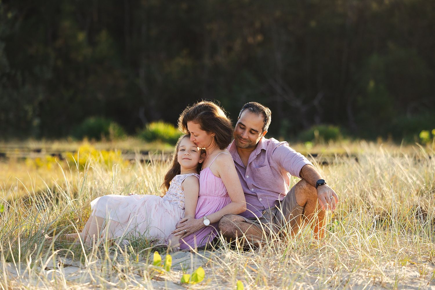 A loving family relaxes together in a sun-drenched field of golden grass during a warm afternoon.