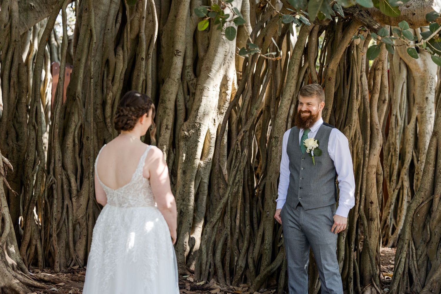 Couple in wedding attire share an intimate first look beside a sprawling banyan tree.