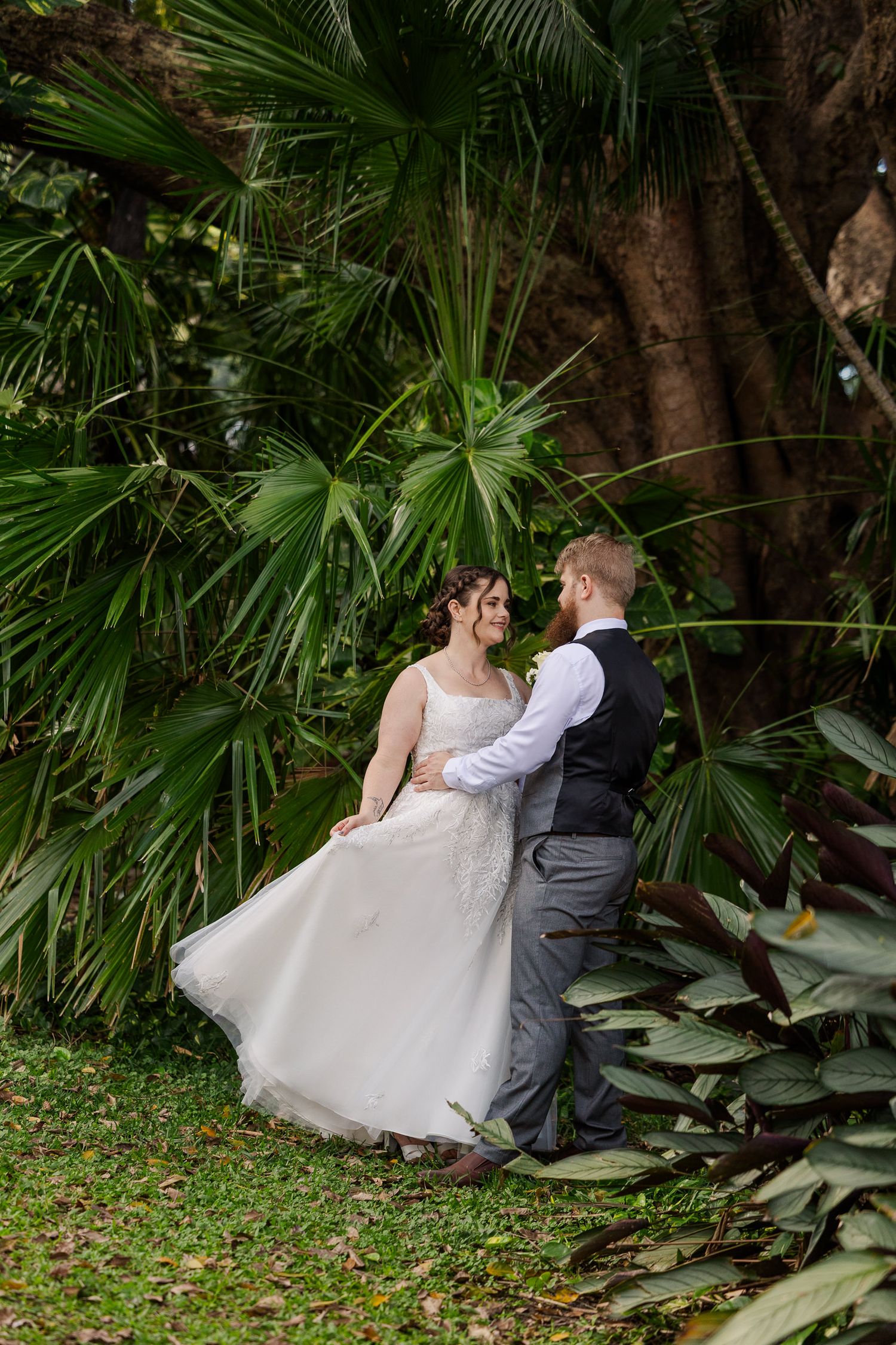A bride and groom share a romantic dance surrounded by lush tropical greenery on their wedding day.