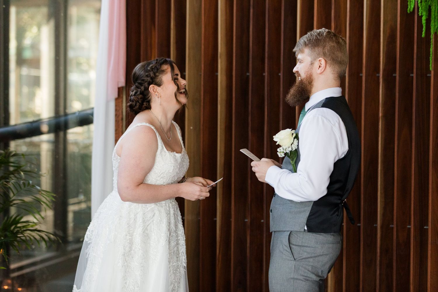 Bride and groom exchanging personal vows, holding notes, smiling joyfully at indoor wedding ceremony.